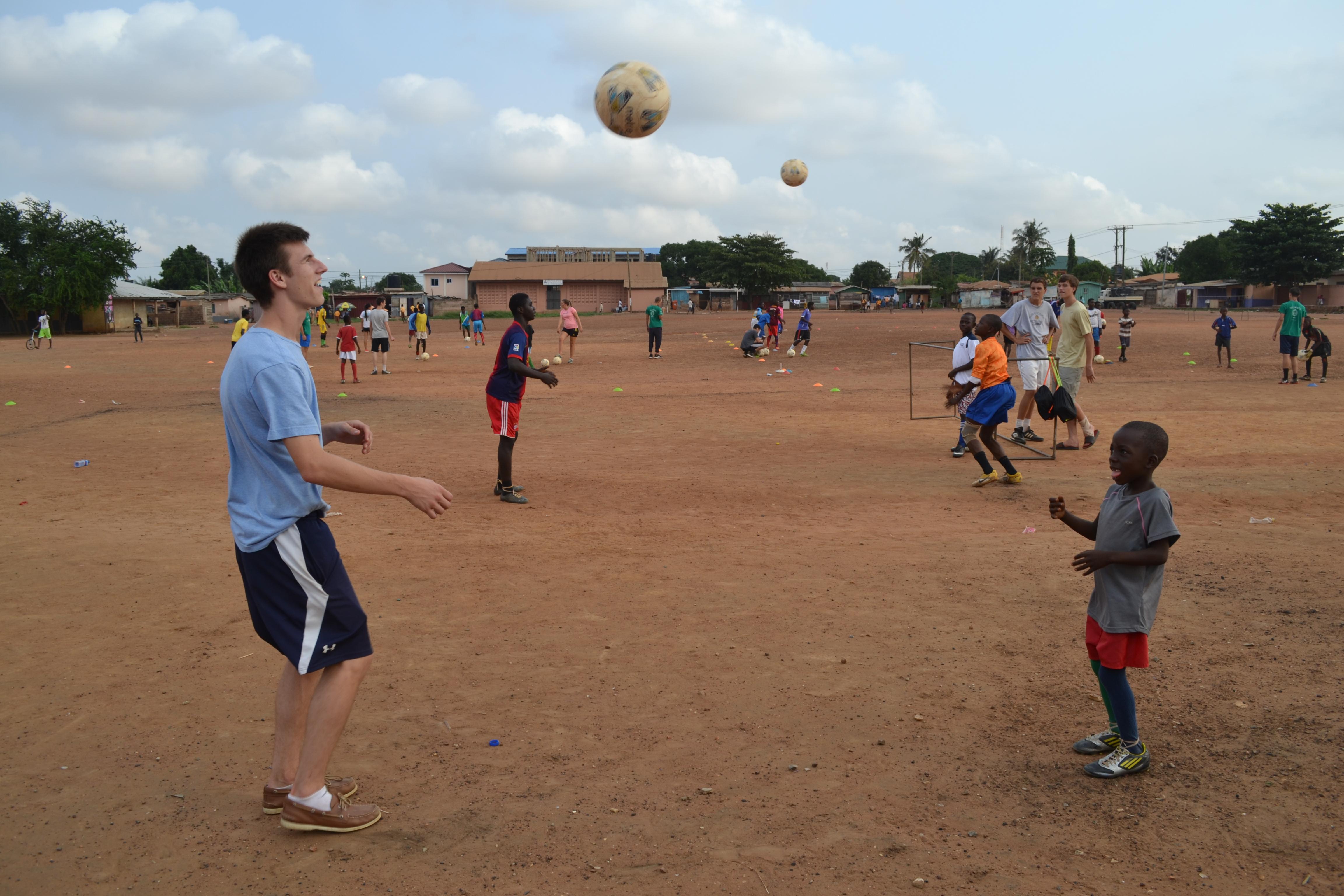A teenage football volunteer coach in Ghana practises ball skills with a young player on a local pitch. Projects Abroad volunteers taking part in football coaching for high school students in Ghana lead a ball skills practice session with a young team.